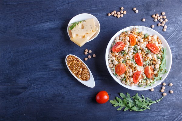 Vegetarian salad of boiled chickpeas, cheese, arugula, mustard and cherry tomatoes on black wooden background. copy space, top view