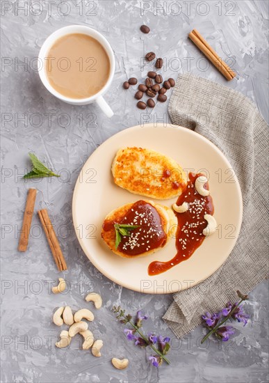 Cheese pancakes with caramel sauce on a beige ceramic plate and a cup of coffee on a gray concrete background. top view, flat lay