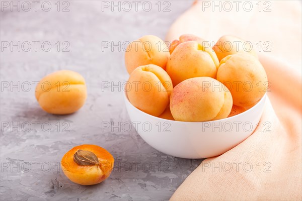 Fresh orange apricots in white bowl on gray concrete background. side view, selective focus