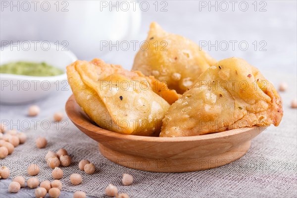 Traditional indian food samosa in wooden plate with mint chutney on a gray concrete background. side view, close up