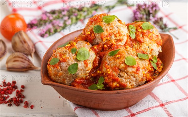 Pork meatballs with tomato sauce, oregano leaves, spices and herbs in clay bowl on a white wooden background with linen textile. side view, close up, selective focus