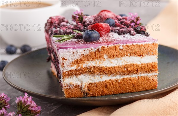 Berry cake with milk cream and blueberry jam on blue ceramic plate with cup of coffee and fresh blueberries on a gray concrete background with orange textile. side view, close up, selective focus