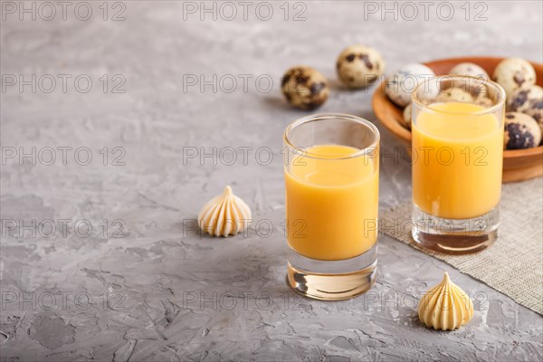 Sweet egg liqueur in glass with quail eggs and meringues on a gray concrete background. Side view, copy space