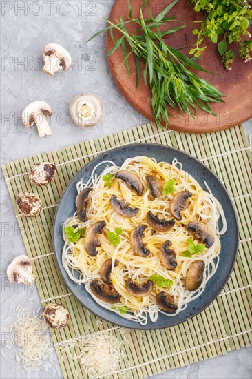 Rice noodles with champignons mushrooms, egg sauce and oregano on blue ceramic plate on a gray concrete background. Top view, flat lay, close up