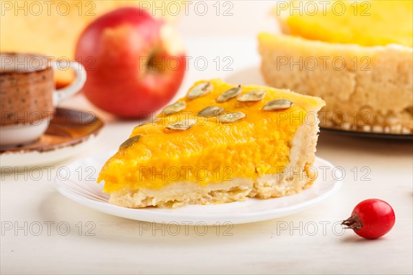 Traditional american sweet pumpkin pie decorated with hawthorn red berries and pumpkin seeds with cup of coffee on a white wooden background. side view, close up, selective focus