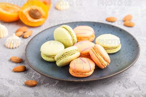 Orange and green macarons or macaroons cakes on blue ceramic plate on a gray concrete background. side view, close up, selective focus