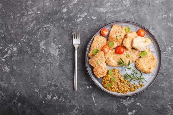 Fried pork chops with tomatoes and herbs on a gray ceramic plate on a black concrete background. top view, flat lay, copy space