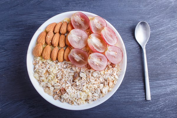 A plate with muesli, almonds, pink grapes on a black wooden background. top view