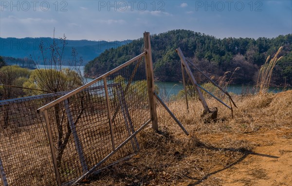 Broken metal gate and post sitting in field with lake and mountains in background on spring afternoon in South Korea