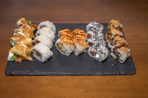 A slate plate hosting a variety of sushi rolls with different toppings and sauces, Majorca, Balearic Islands, Spain, Europe