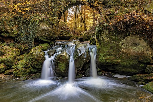 The three-armed Schiessentuempel waterfall in the Mullerthal in Luxembourg in sunny autumn weather as a long exposure