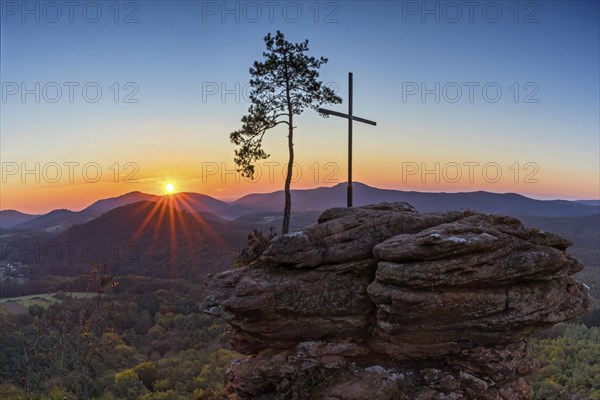 Sunrise on the Roetzenfelsen in the Palatinate Forest with bright sunshine and the lone pine tree and the summit cross on the red rock