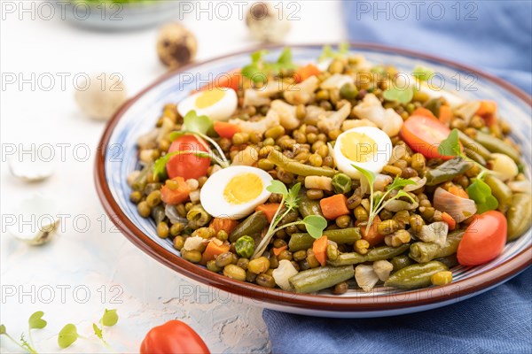 Mung bean porridge with quail eggs, tomatoes and microgreen sprouts on a white concrete background and blue textile. Side view, close up, selective focus