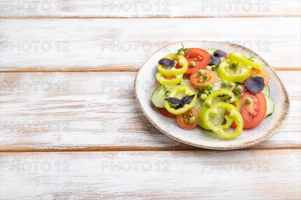 Vegetarian salad from green pea, tomatoes, pepper and basil on white wooden background. Side view, copy space, close up