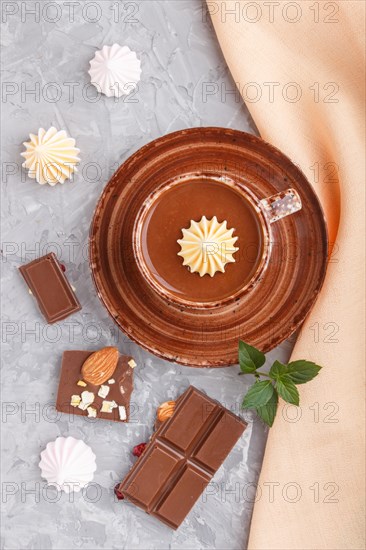 Cup of hot chocolate and pieces of milk chocolate with almonds on a gray concrete background with orange textile. top view, flat lay, close up