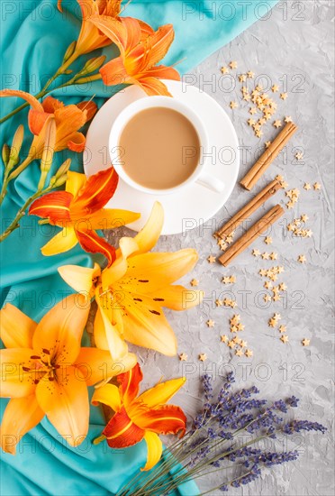 Orange day-lily and lavender flowers and a cup of coffee on a gray concrete background, with blue textile. Morninig, spring, fashion composition. Flat lay, top view