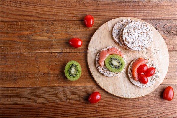 Rice cakes with salmon, kiwi and cherry tomatoes on wooden background. top view, copy space
