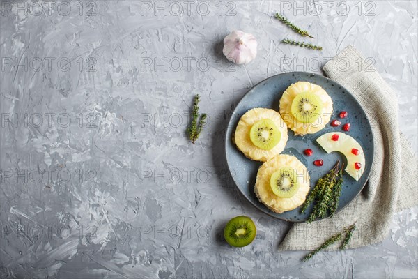 Pieces of baked pork with pineapple, cheese and kiwi on gray background, top view, copy space