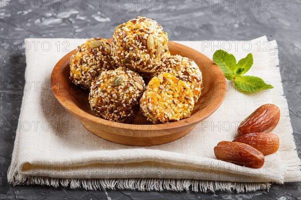 Energy ball cakes with dried apricots, sesame, linen, walnuts and dates with green mint leaves in a wooden bowl on a black concrete background. linen napkin, side view, close up. vegan homemade candy