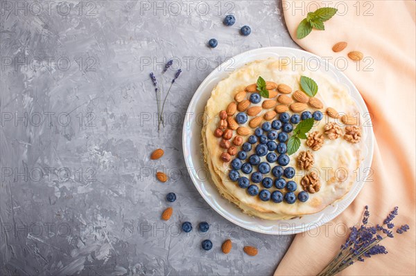 Homemade layered Napoleon cake with milk cream. Decorated with blueberry, almonds, walnuts, hazelnuts, mint on a gray concrete background and orange textile. top view. flat lay, copy space