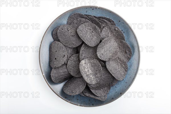 Black potato chips with charcoal on a blue ceramic plate isolated on white background. Top view, flat lay, close up