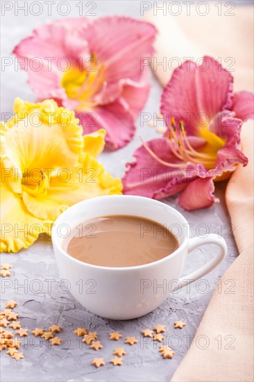 Yellow anf purple day-lilies cup of coffee on a gray concrete background, with orange textile. Morninig, spring, fashion composition, side view, close up, selective focus