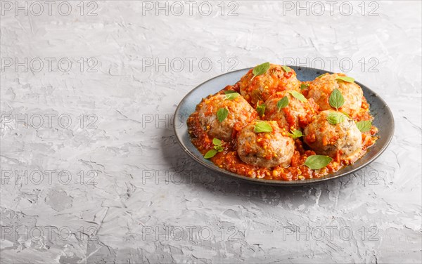 Pork meatballs with tomato sauce, oregano leaves, spices and herbs on blue ceramic plate on a gray concrete background. side view, copy space