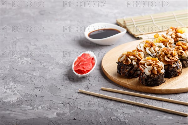 Japanese maki sushi rolls with cream cheese, chopsticks, soy sauce and marinated ginger on wooden board on a gray concrete background. Side view, copy space, selective focus