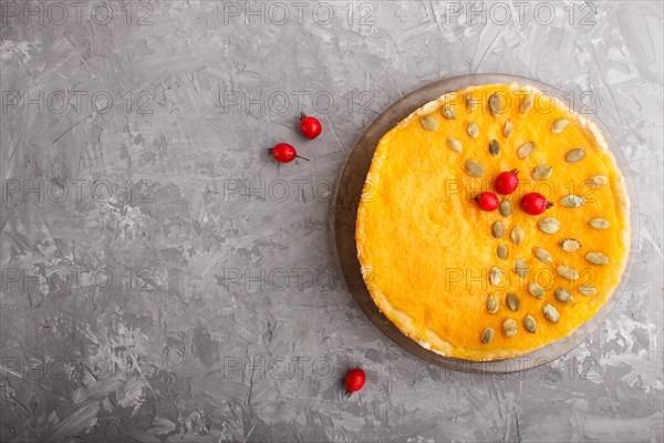 Traditional american sweet pumpkin pie decorated with hawthorn red berries and pumpkin seeds on a gray concrete background. top view, flat lay, copy space