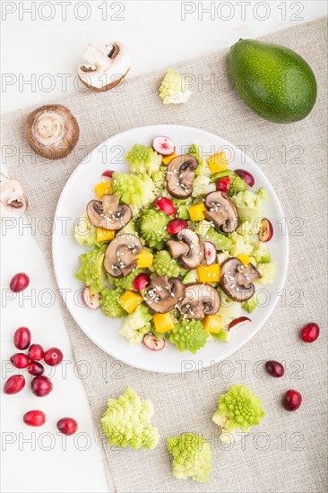 Vegetarian salad from romanesco cabbage, champignons, cranberry, avocado and pumpkin on a white wooden background and linen textile. top view, close up, flat lay