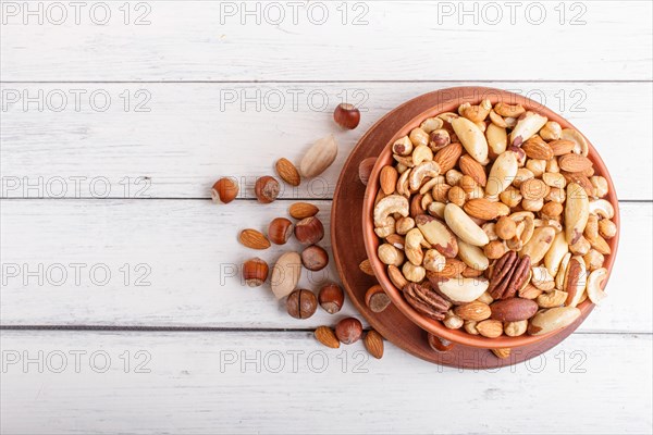 Mixed different kinds of nuts in ceramic bowl on white wooden background with copy space. hazelnut, brazil nut, almond, pumpkin seeds, cashew. top view