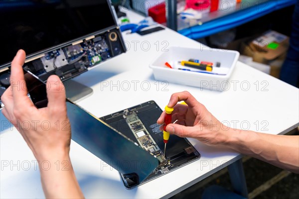 Close-up photo with elevated view of a male engineer fixing a digital tablet on a repair workshop