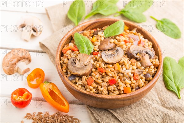 Spelt (dinkel wheat) porridge with vegetables and mushrooms in wooden bowl on a white wooden background and linen textile. Side view, selective focus. Russian traditional cuisine