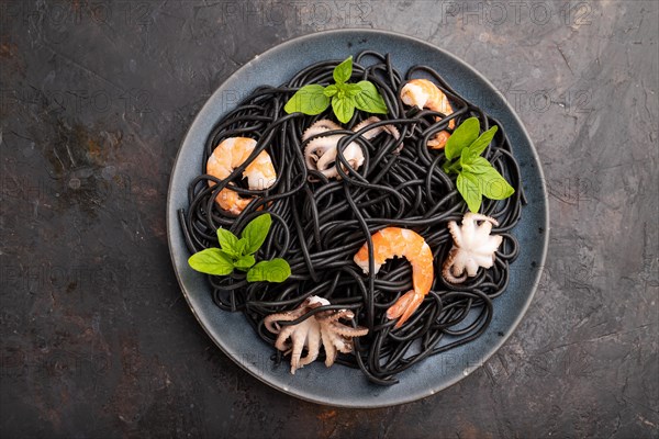 Black cuttlefish ink pasta with shrimps or prawns and small octopuses on black concrete background. Top view, flat lay, close up