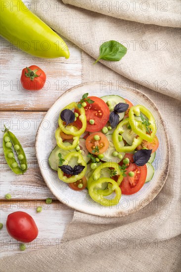 Vegetarian salad from green pea, tomatoes, pepper and basil on white wooden background and linen textile. top view, close up, flat lay