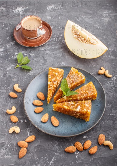 Traditional turkish candy cezerye made from caramelised melon, roasted walnuts, hazelnuts, cashew, pistachios in blue ceramic plate and a cup of coffee on a black concrete background. side view, close up