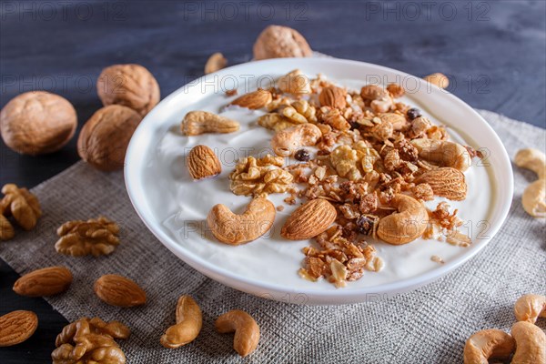 White plate with greek yogurt, granola, almond, cashew, walnuts on black wooden background. close up