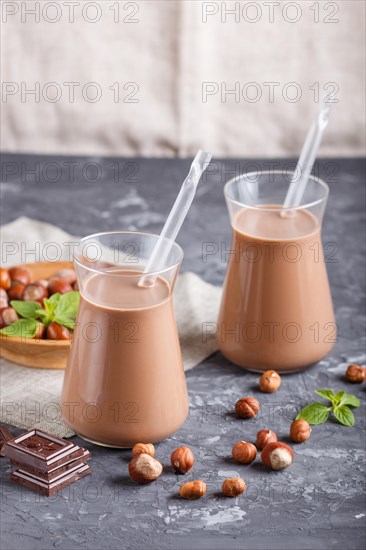 Organic non dairy hazelnut chocolate milk in glass and wooden plate with hazelnuts on a black concrete background. Vegan healthy food concept, close up, side view