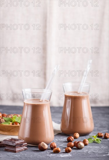 Organic non dairy hazelnut chocolate milk in glass and wooden plate with hazelnuts on a black concrete background. Vegan healthy food concept, close up, side view, copy space