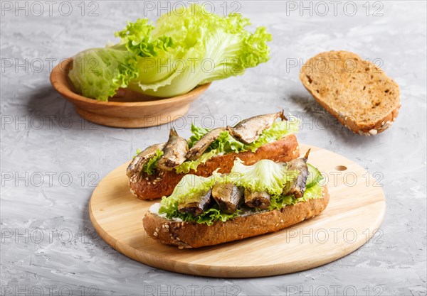 Sprats sandwiches with lettuce and cream cheese on wooden board on a gray concrete background. side view, close up