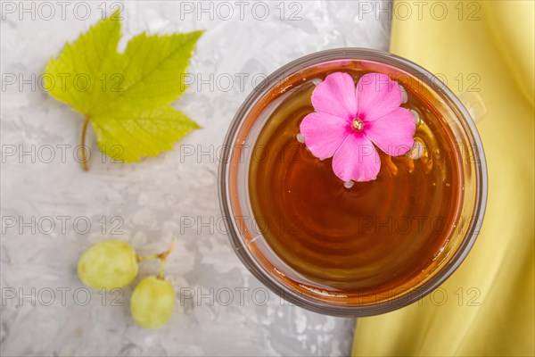 Glass of green grape juice with green textile and pink flower on a gray concrete background. Morninig, spring, healthy drink concept. Top view, close up, flat lay