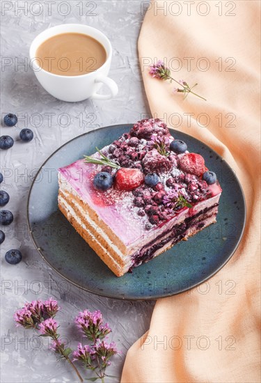 Berry cake with milk cream and blueberry jam on blue ceramic plate with cup of coffee and fresh blueberries on a gray concrete background with orange textile. side view, close up