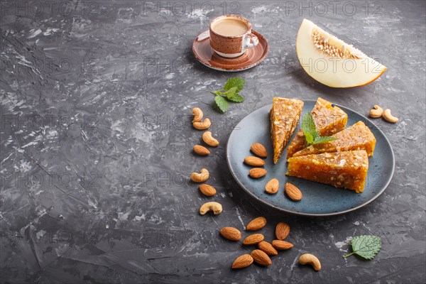 Traditional turkish candy cezerye made from caramelised melon, roasted walnuts, hazelnuts, cashew, pistachios in blue ceramic plate and a cup of coffee on a black concrete background. side view, close up, copy space