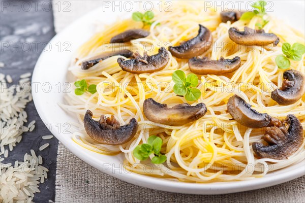 Rice noodles with champignons mushrooms, egg sauce and oregano on white ceramic plate on a black concrete background. side view, selective focus, close up