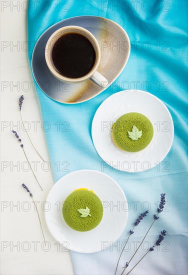 Green mousse cake with pistachio cream and a cup of coffee on a white wooden background and blue textile. top view, flat lay, close up