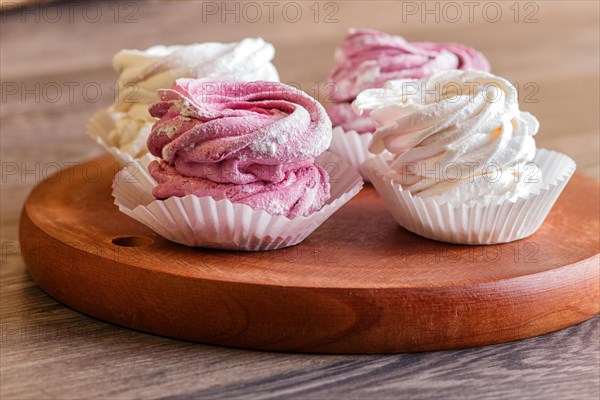 Pink and white marshmallows on a round wooden board on a gray wooden background. selective focus