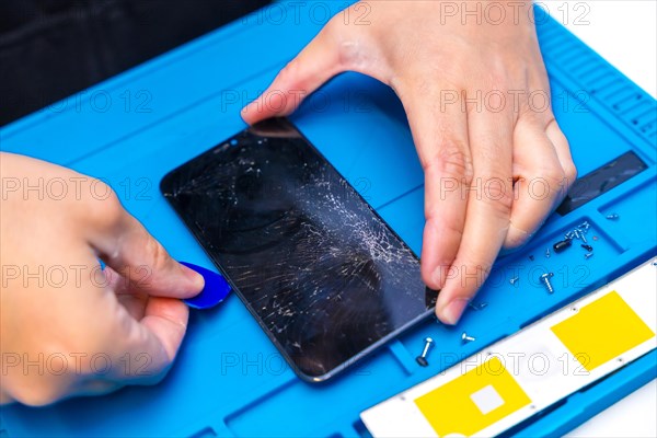 Close-up top view of a male technician uses a pick to open the screen of a mobile phone in a repair shop