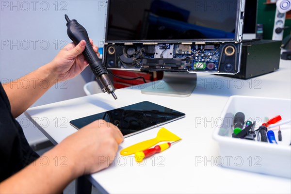 Side view of an unrecognizable technician fixing a computer component using a soldering iron in a workshop