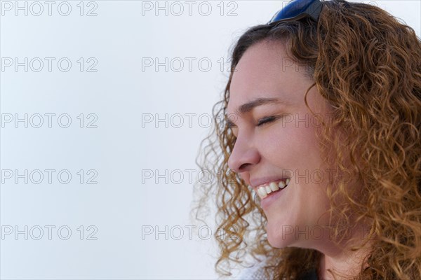 Attractive woman with long curly hair seen in profile smiling with closed eyes on white background and copy space