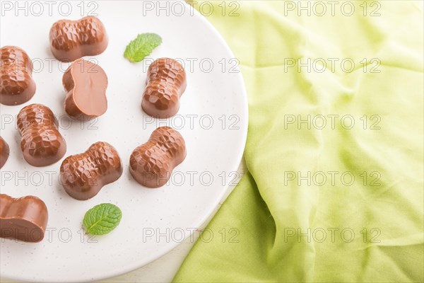 Chocolate candies with almonds on a white wooden background and green textile. side view, close up, selective focus
